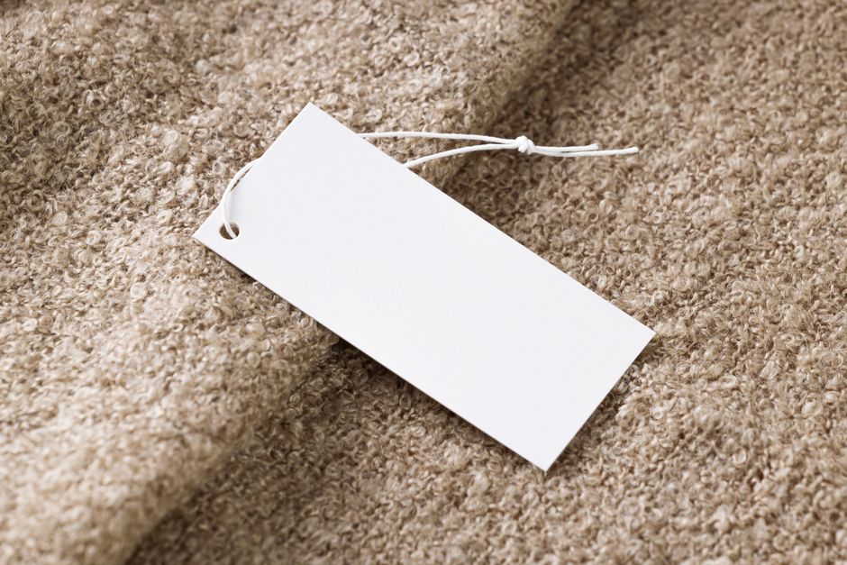 Close-up of a blank white price tag on textured beige fabric, ideal for branding use.